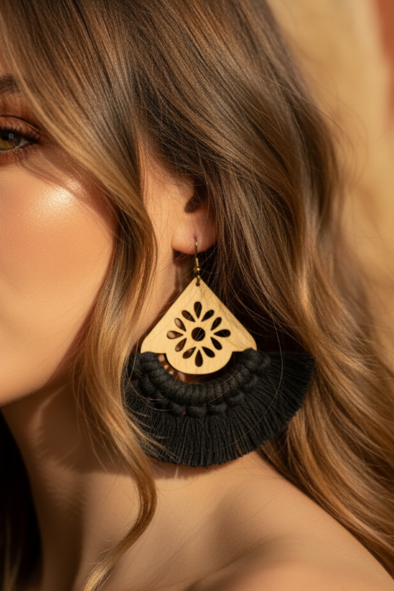 Close-up of a woman wearing a wooden earring with black tassels against a neutral background
