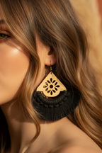 Close-up of a woman wearing a wooden earring with black tassels against a neutral background