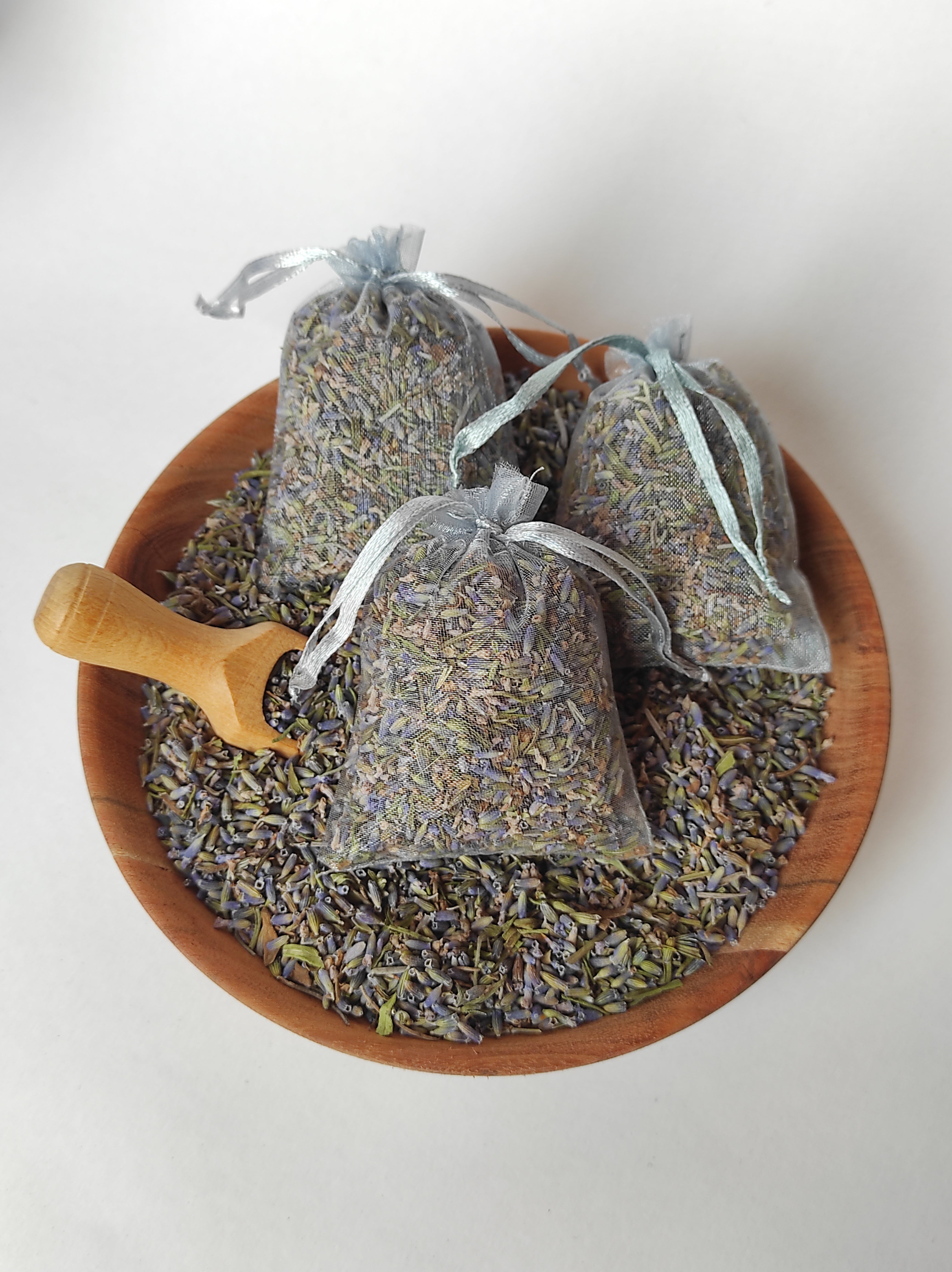 Wooden bowl with lavender bags and a wooden scoop on a white background
